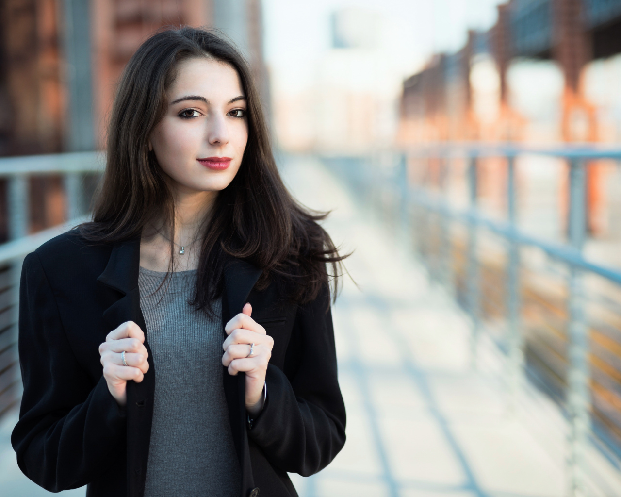 Молодая девушка в черном пальто стоит на мосту