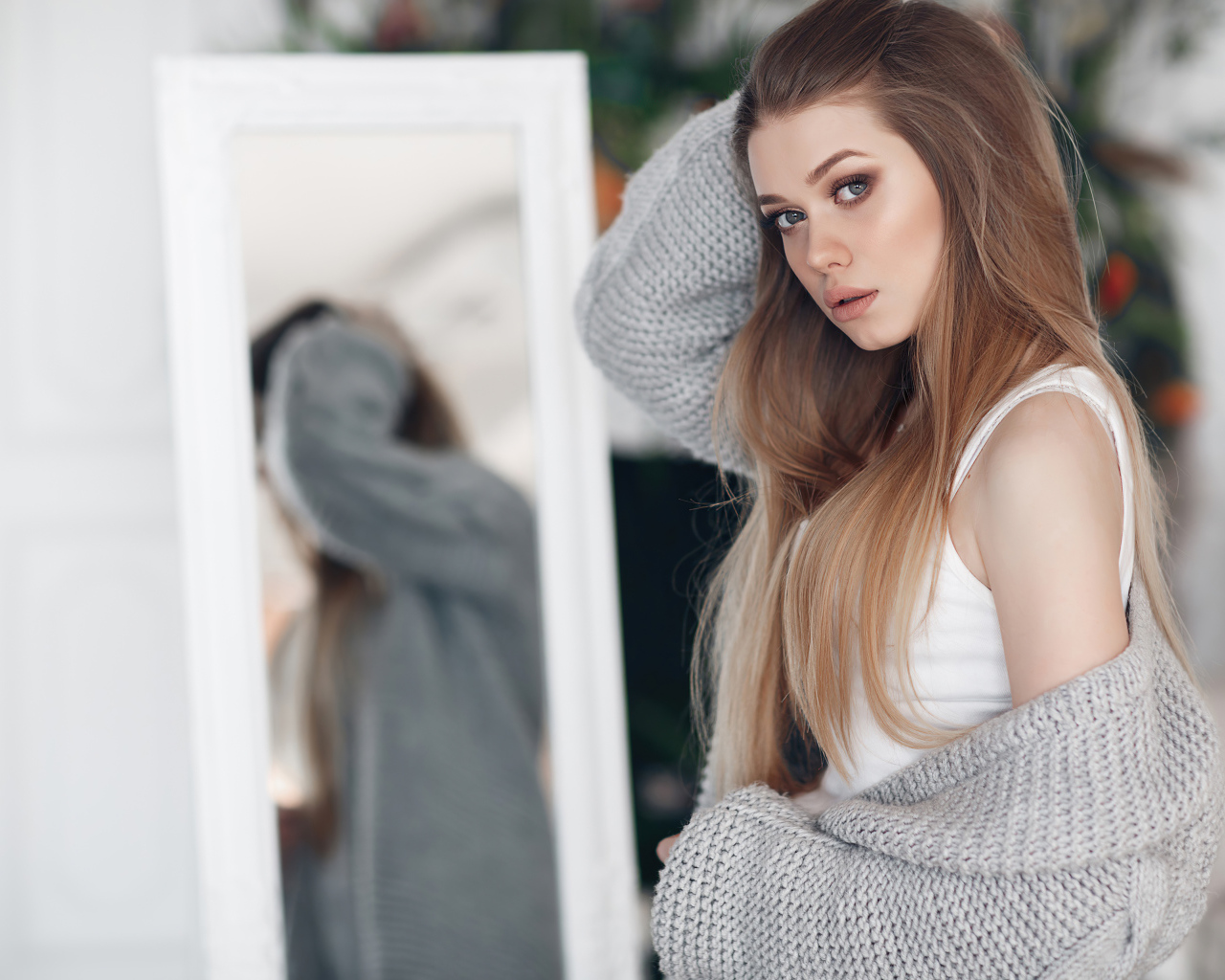 Молодая девушка в серой кофте стоит у зеркала 