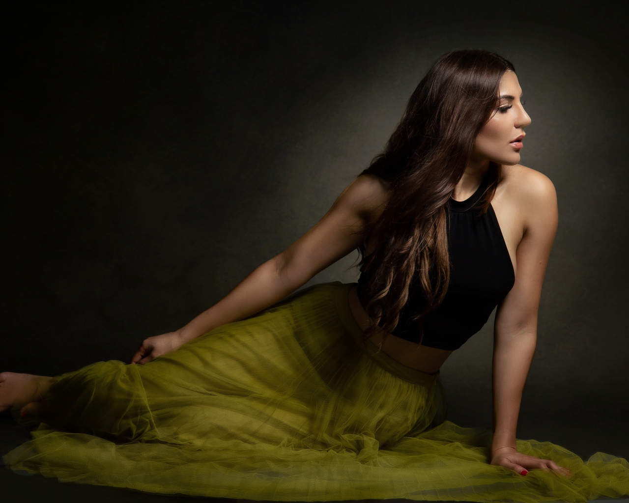 Молодая девушка в длинной юбке сидит на полу