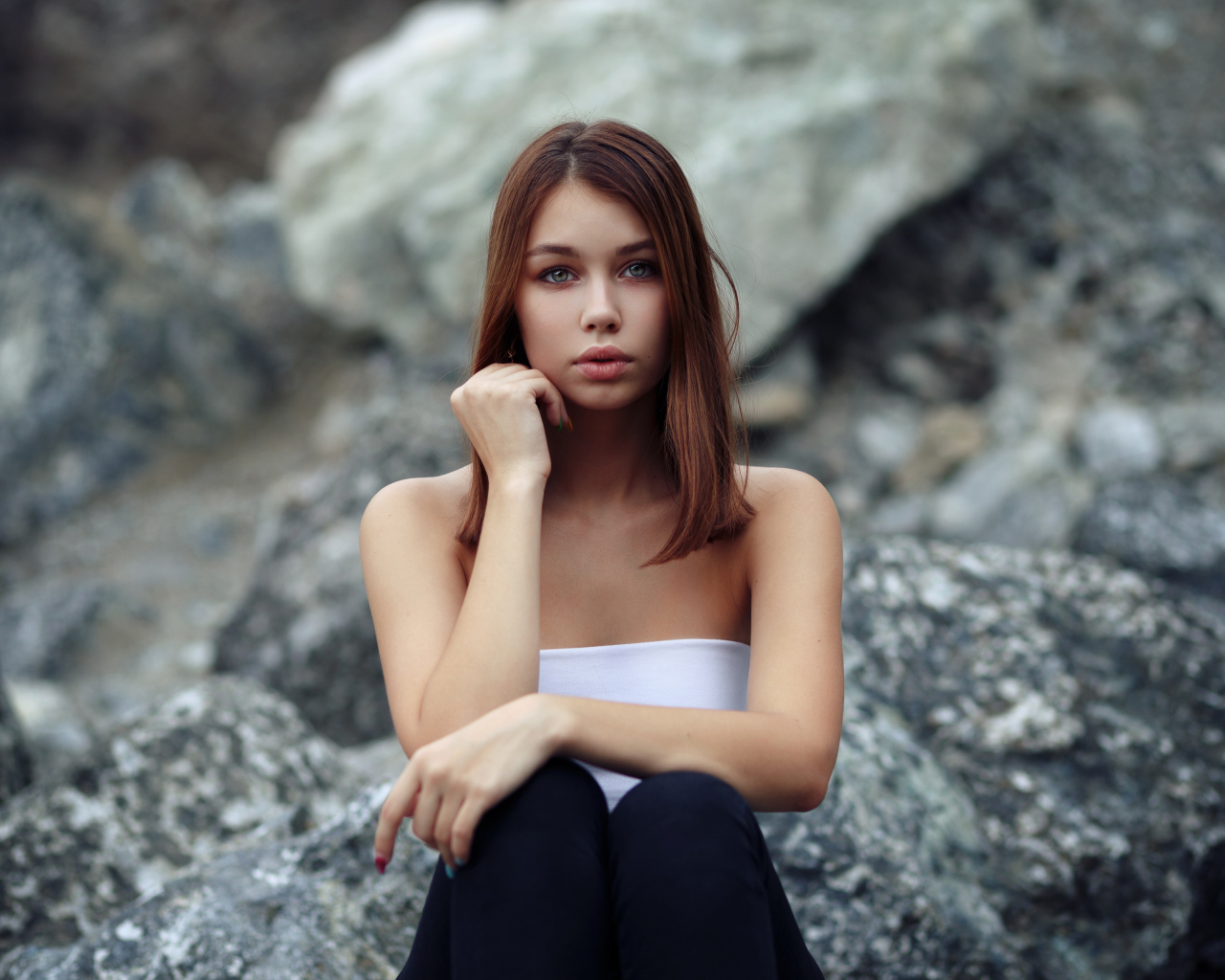 Молодая девушка сидит на камнях 