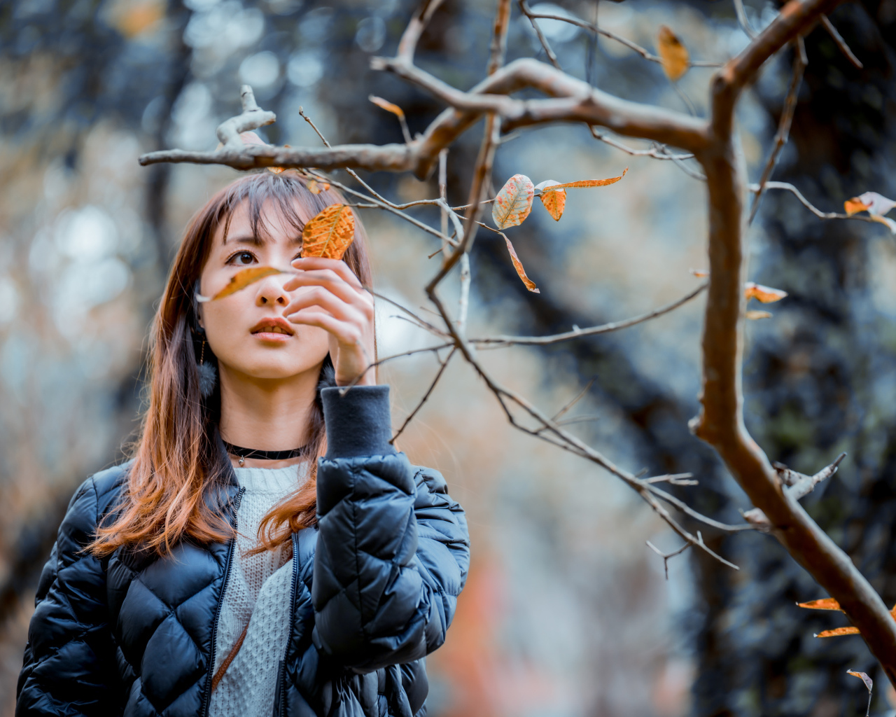 Девушка азиатка в черной куртке у дерева