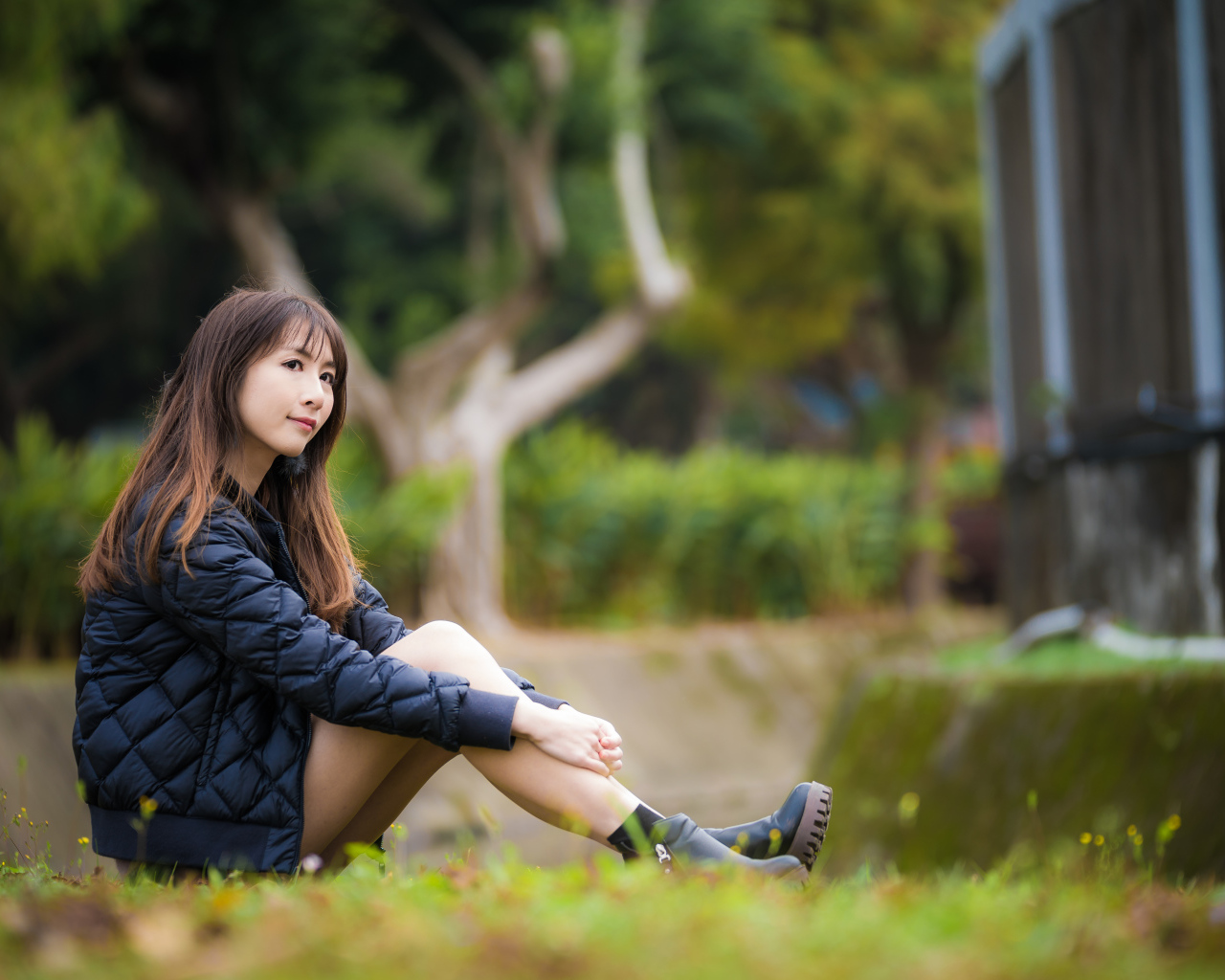 Девушка азиатка в черной куртке сидит на траве