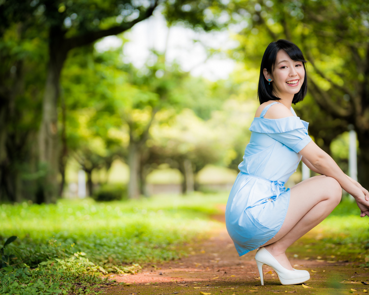 Девушка азиатка в голубом платье сидит на корточках в парке