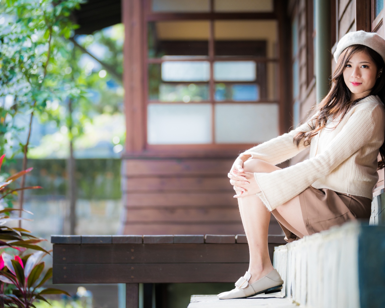 Девушка азиатка в свитере сидит на пороге 