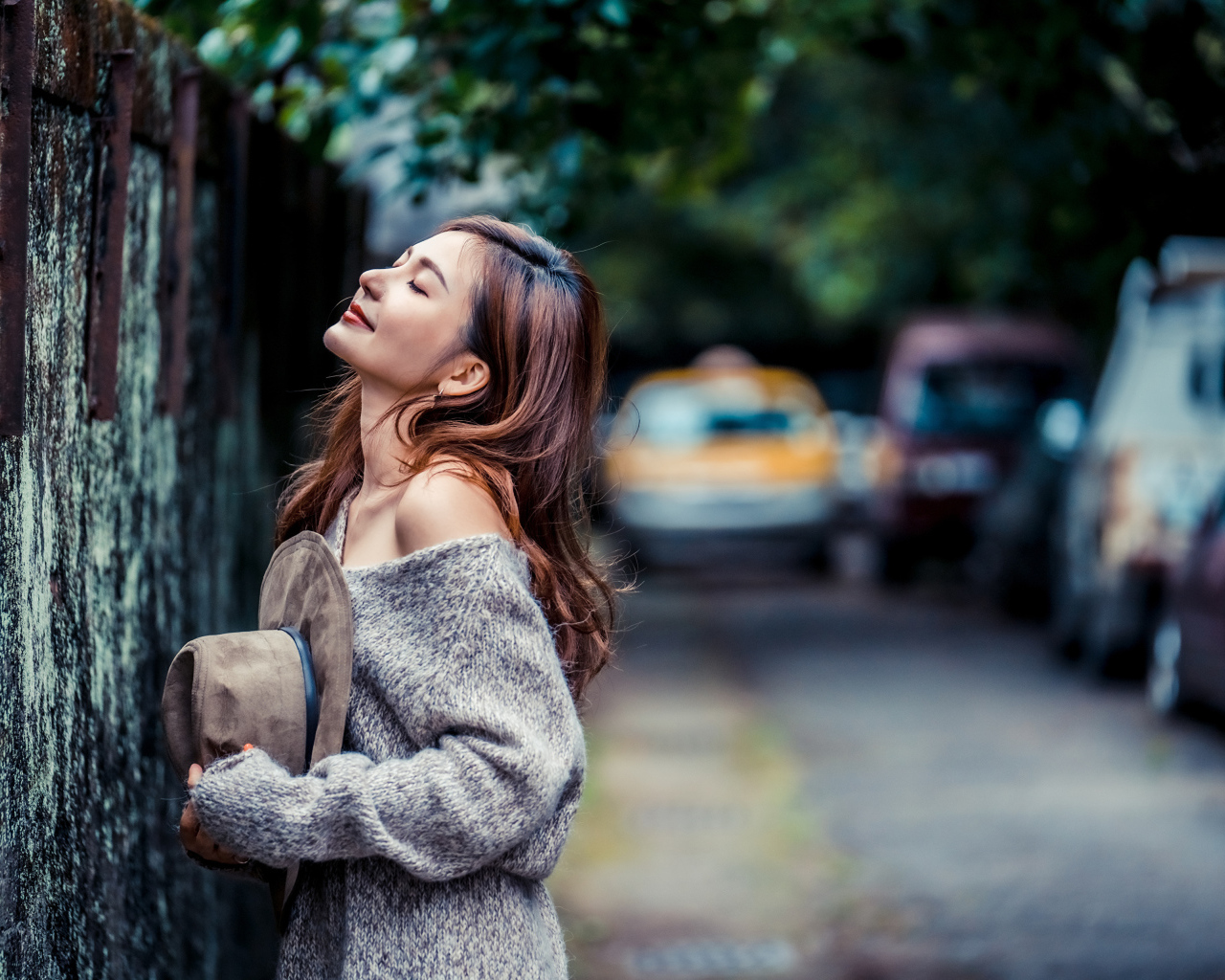 Девушка азиатка в теплом свитере стоит у забора