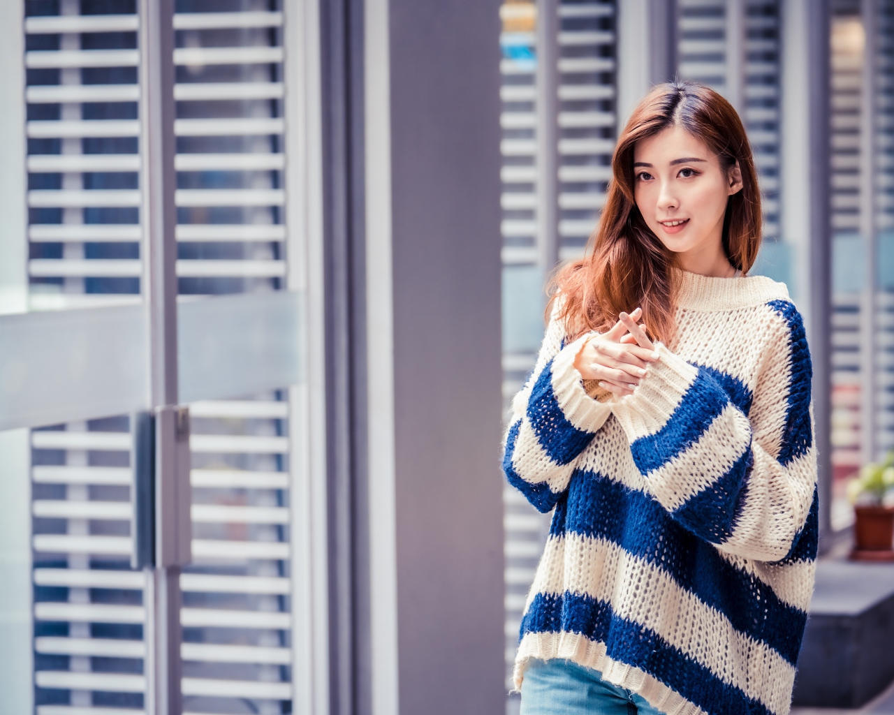 Девушка азиатка в теплом свитере стоит у окна