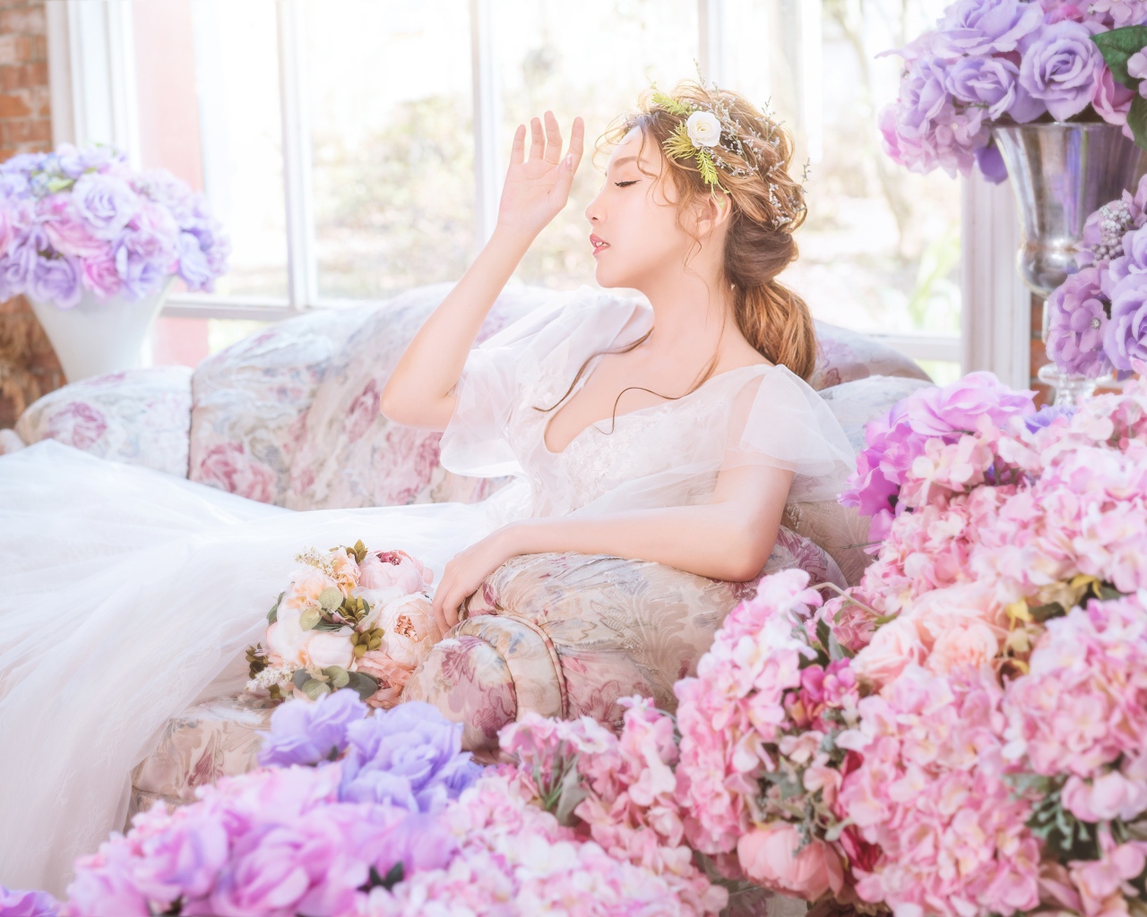 Девушка азиатка в белом платье сидит на диване в комнате с цветами