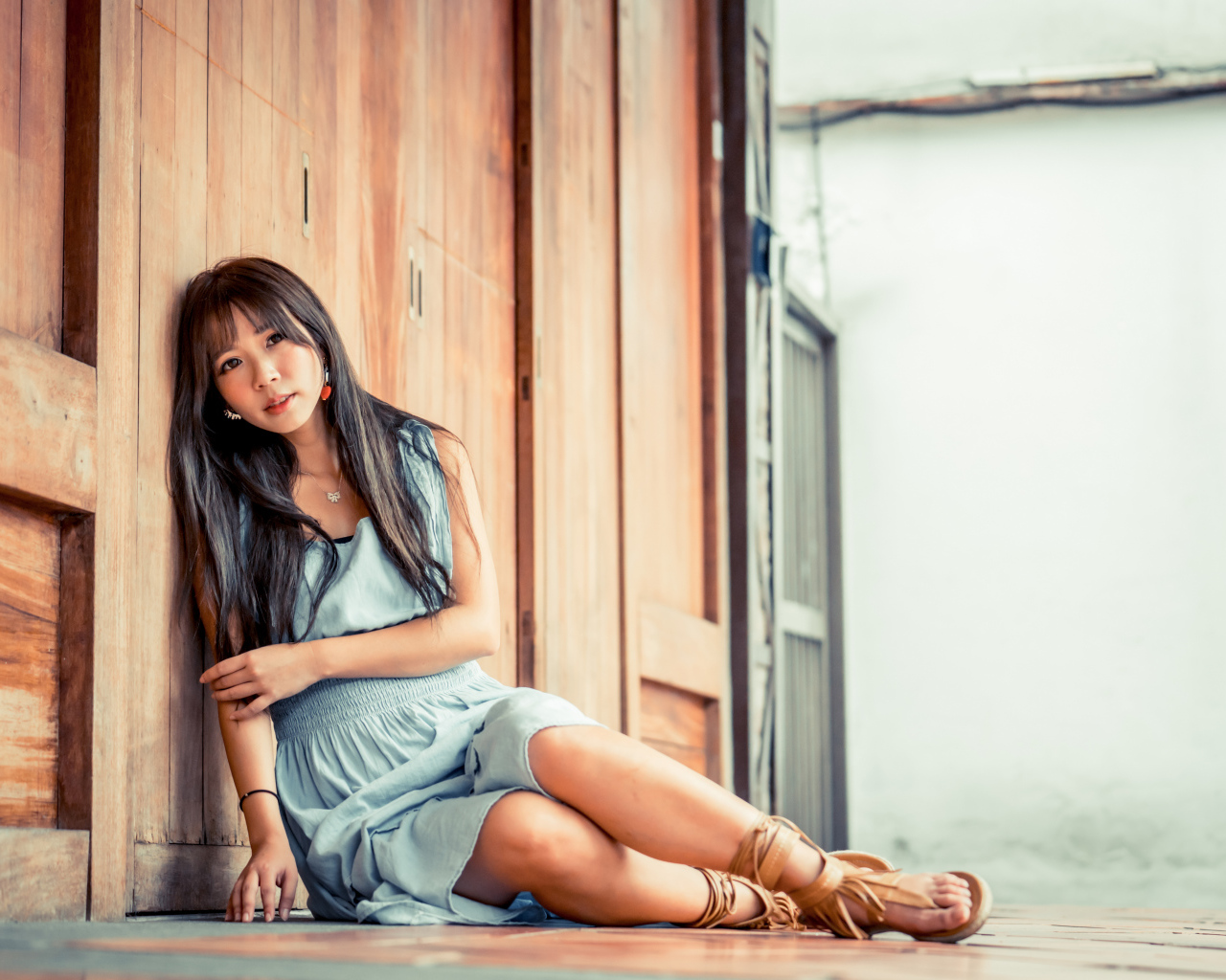 Девушка азиатка в платье сидит на полу у стены 