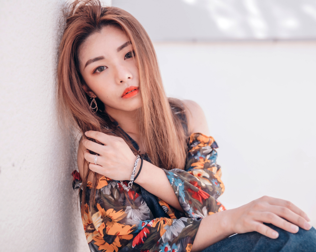 Девушка азиатка сидит на полу у стены 