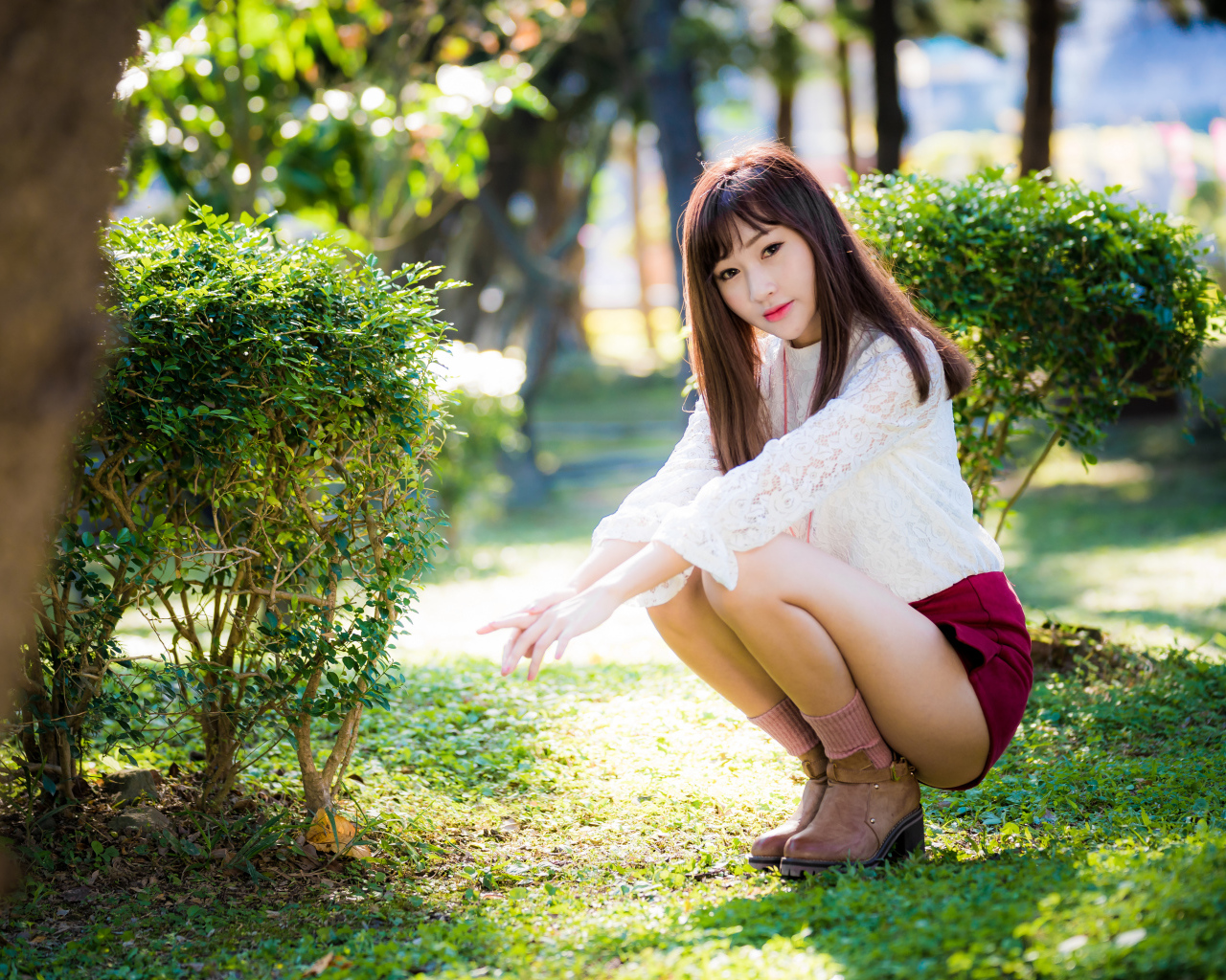 Девушка азиатка сидит на корточках в парке