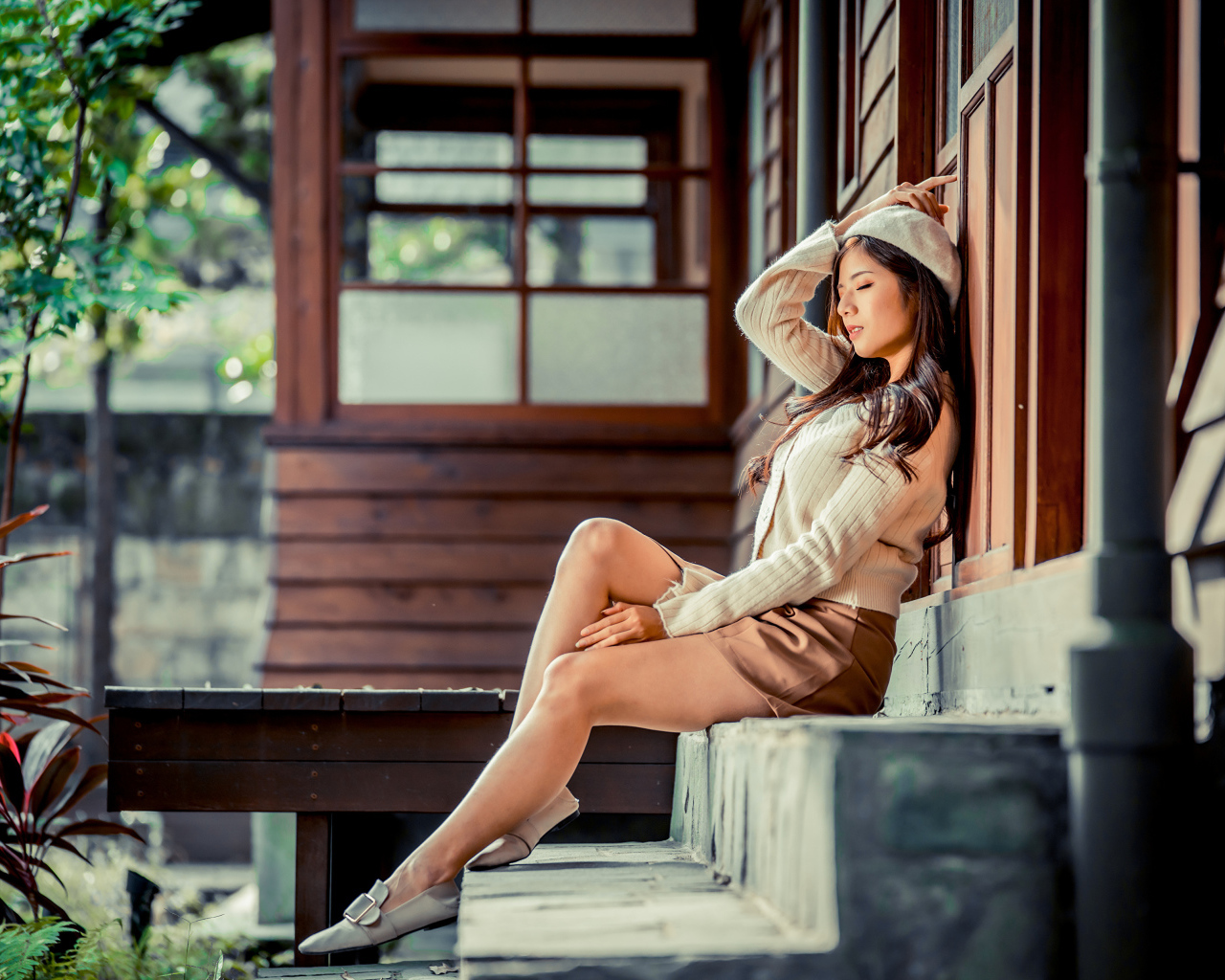 Девушка азиатка с закрытыми глазами сидит на ступеньках дома 