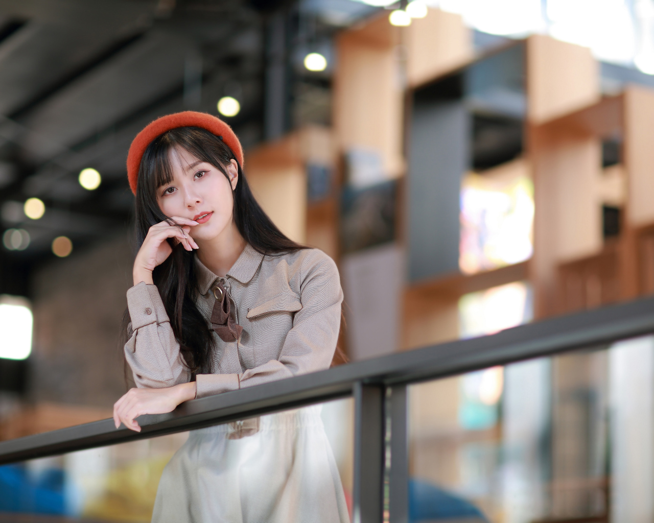 Азиатка в сером платье стоит у перил 