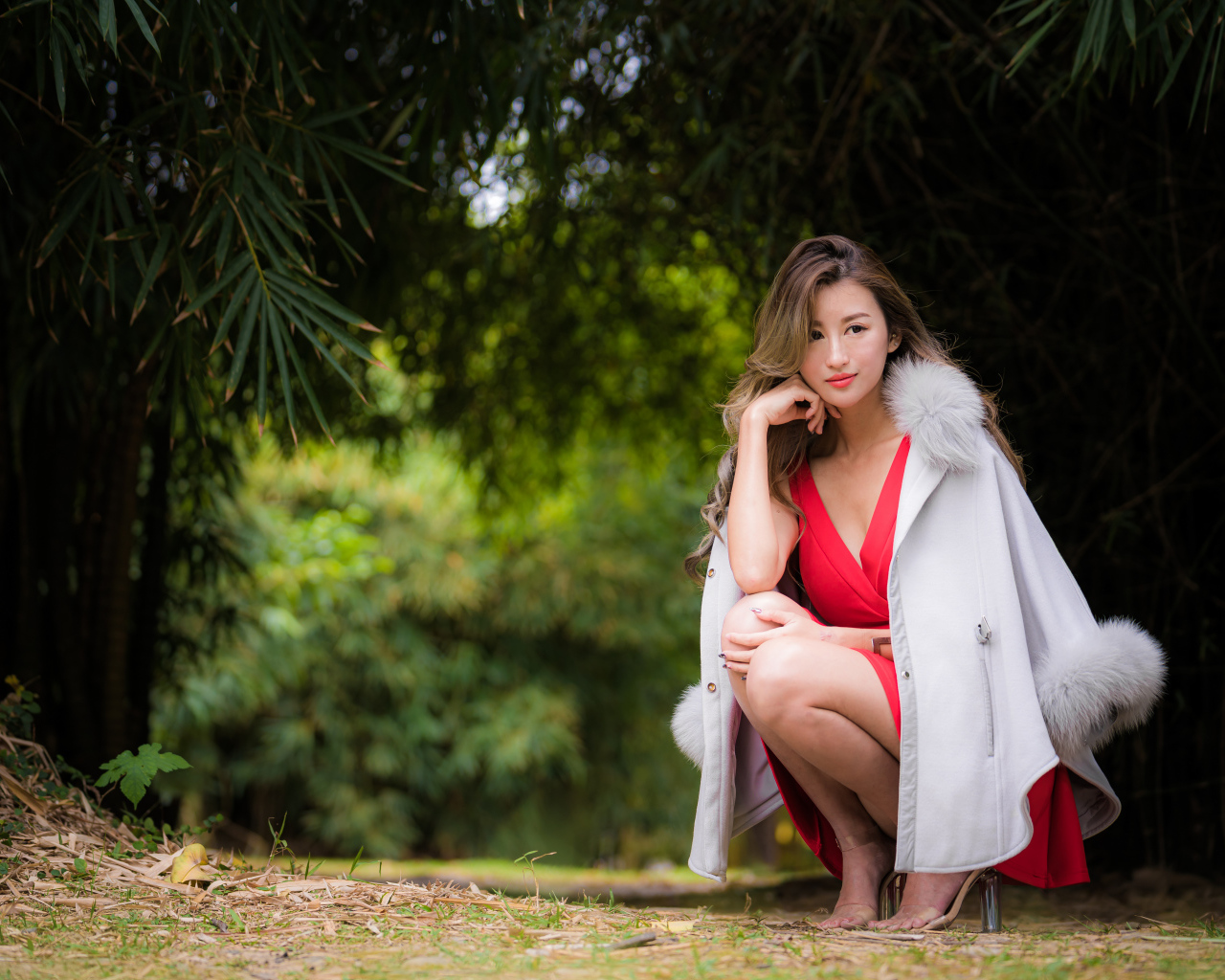 Азиатка в красном платье сидит в парке 