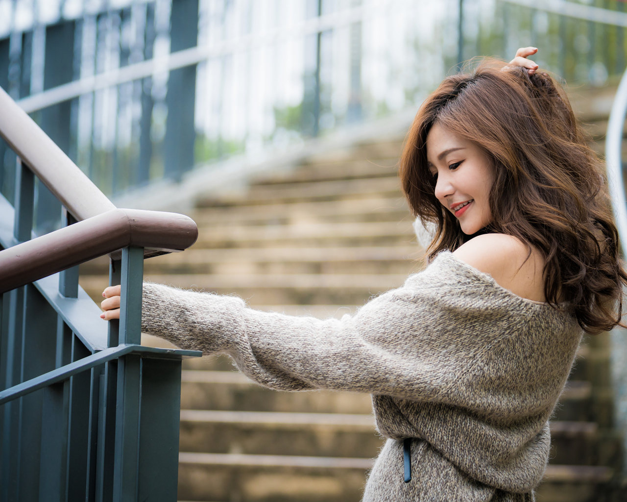 Красивая девушка азиатка в сером свитере на ступеньках 