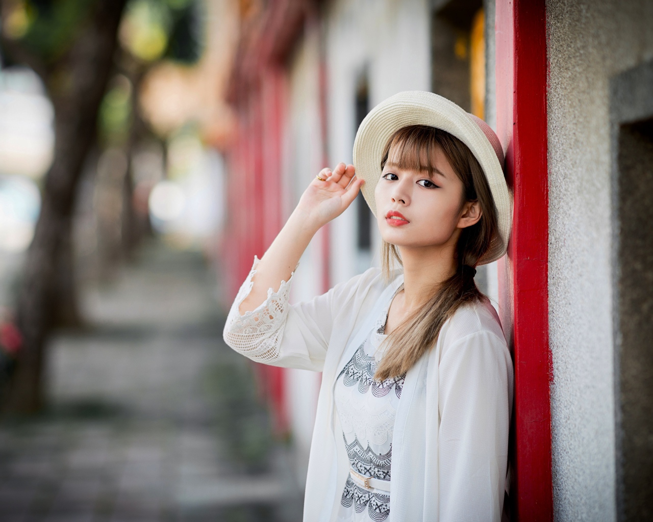 Красивая азиатка в шляпе стоит у стены