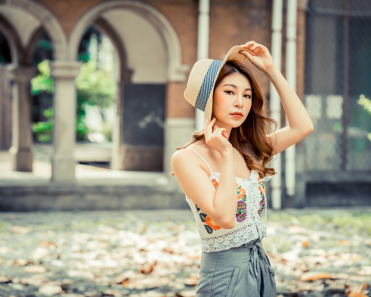 Красивая девушка азиатка в шляпе стоит в парке 