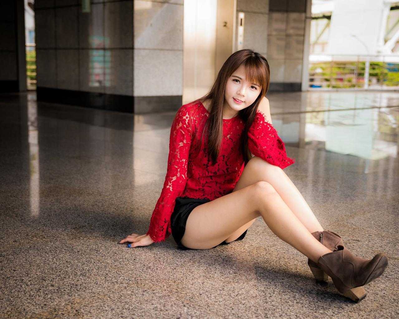 Красивая девушка азиатка в красной блузке сидит на полу