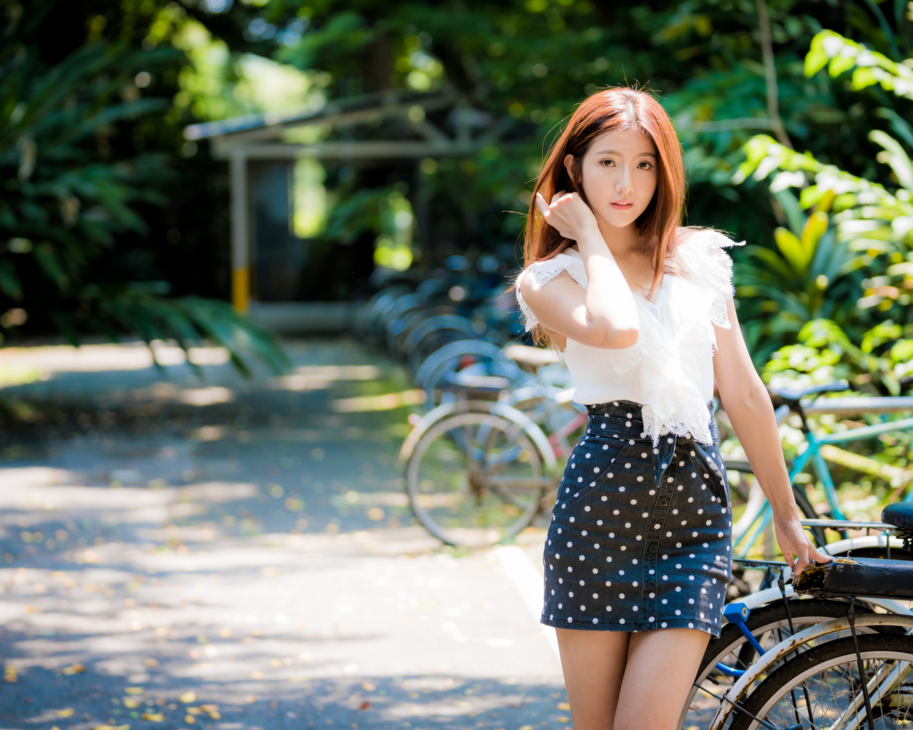 Красивая девушка азиатка в юбке в горох стоит у велосипеда 