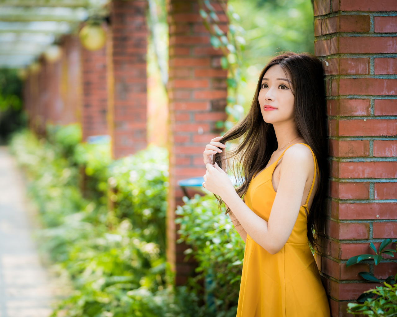 Красивая азиатка в желтом платье стоит у кирпичной колонны 