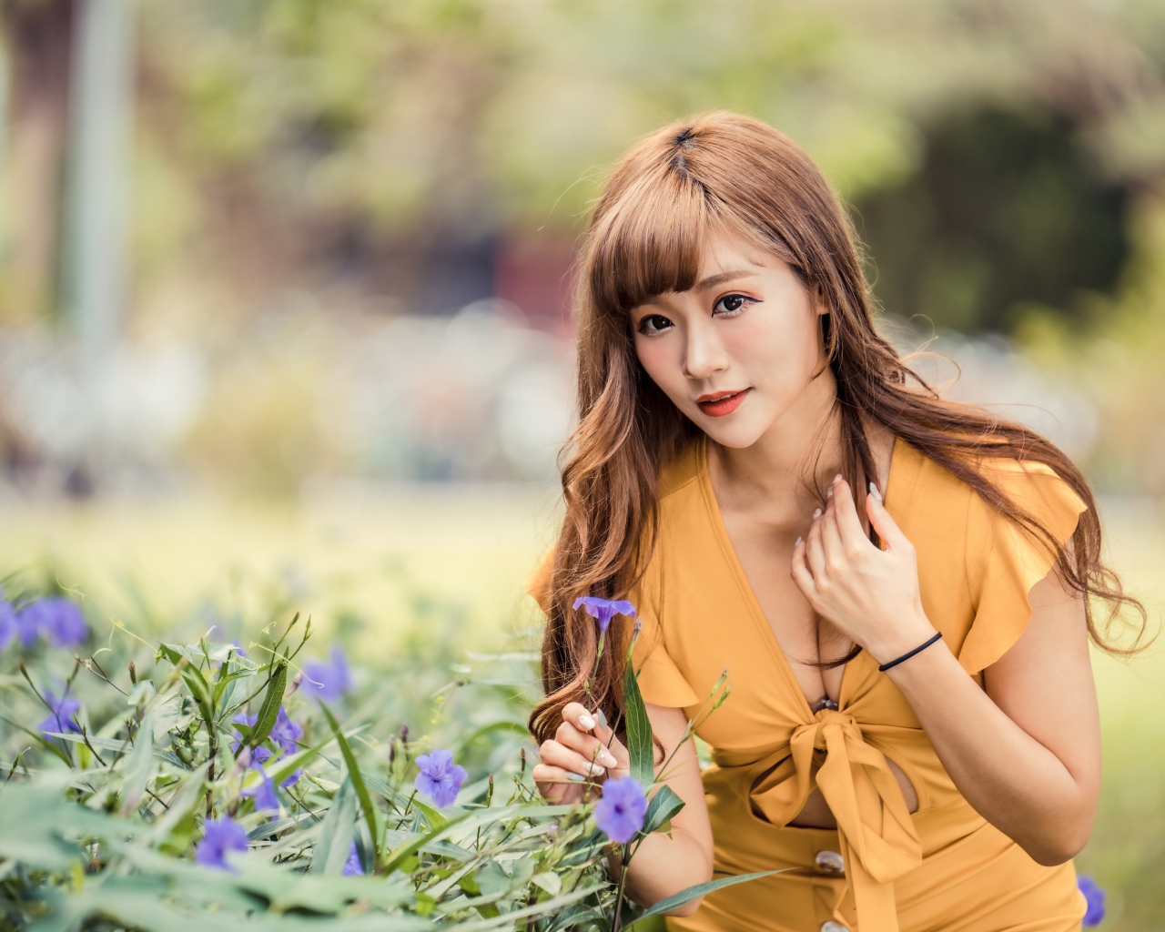 Красивая девушка азиатка в желтом платье у фиолетовых цветов 