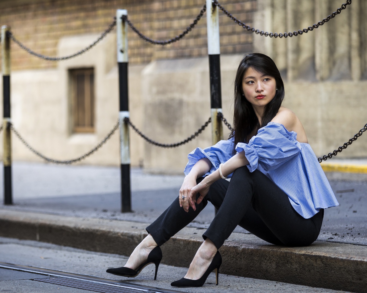 Красивая девушка азиатка в черных брюках сидит на земле