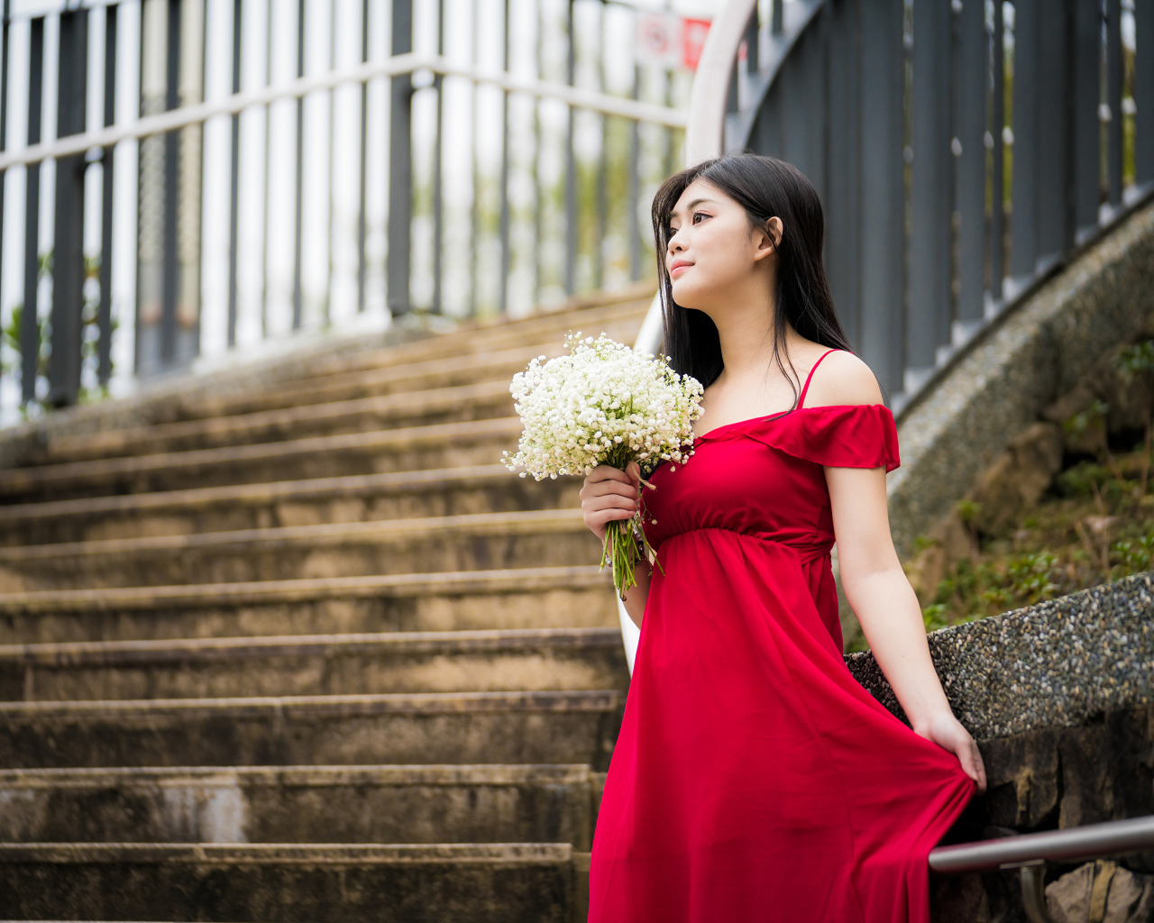 Красивая азиатка в красном платье стоит на ступеньках с букетом ландышей