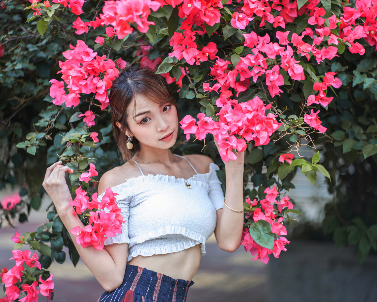 Красивая азиатка стоит у дерева с красными цветами