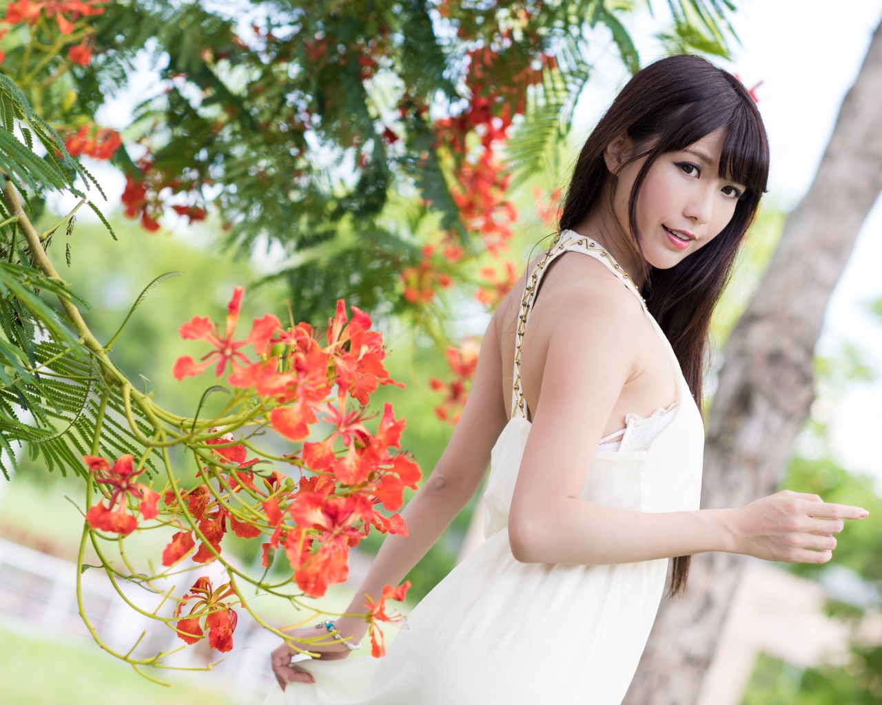 Красивая девушка азиатка в красном платье у дерева с цветами
