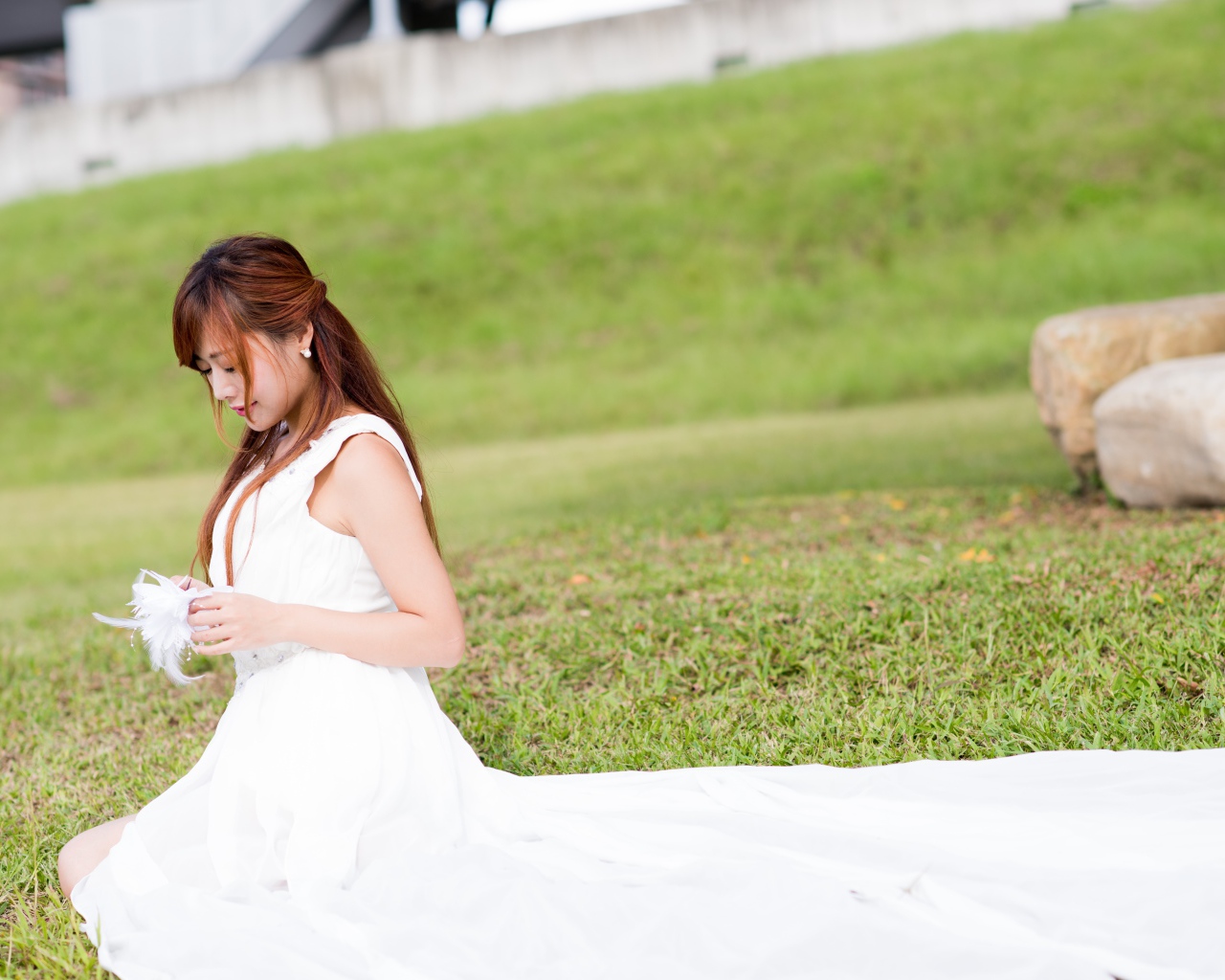 Красивая девушка азиатка в свадебном платье сидит на траве