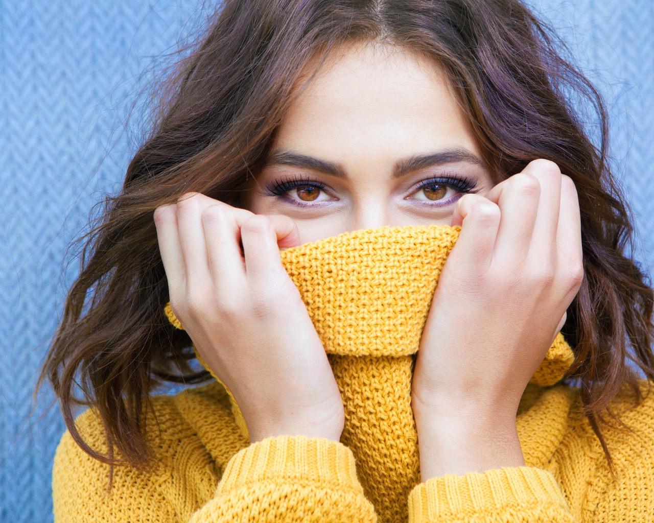 Красивая кареглазая девушка закрывает лицо свитером