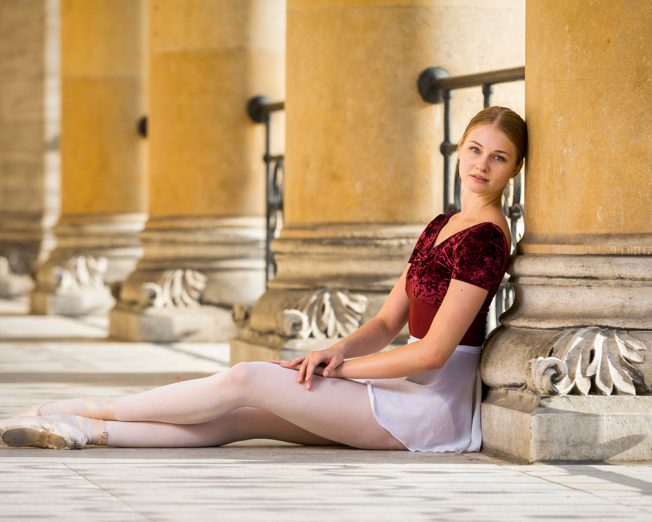Красивая девушка балерина сидит на полу у колонны 