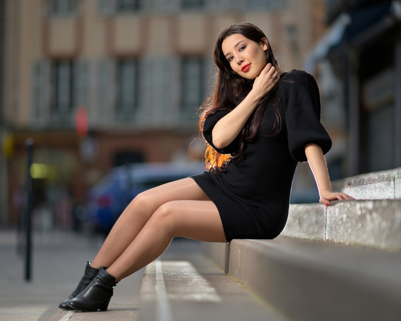 Красивая девушка в черном платье сидит на ступенях