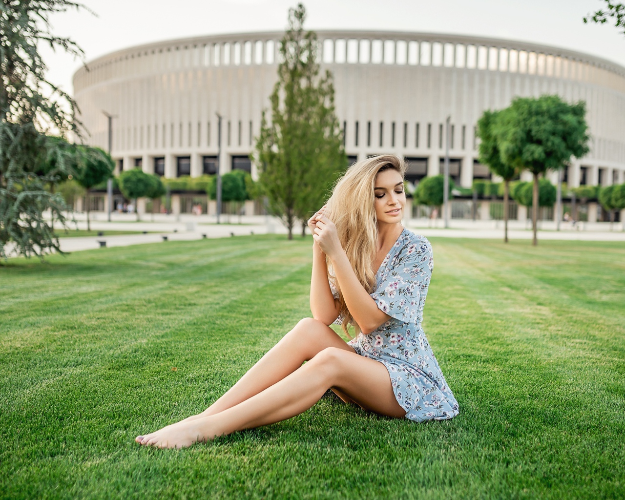 Красивая девушка в платье сидит на зеленом газоне 