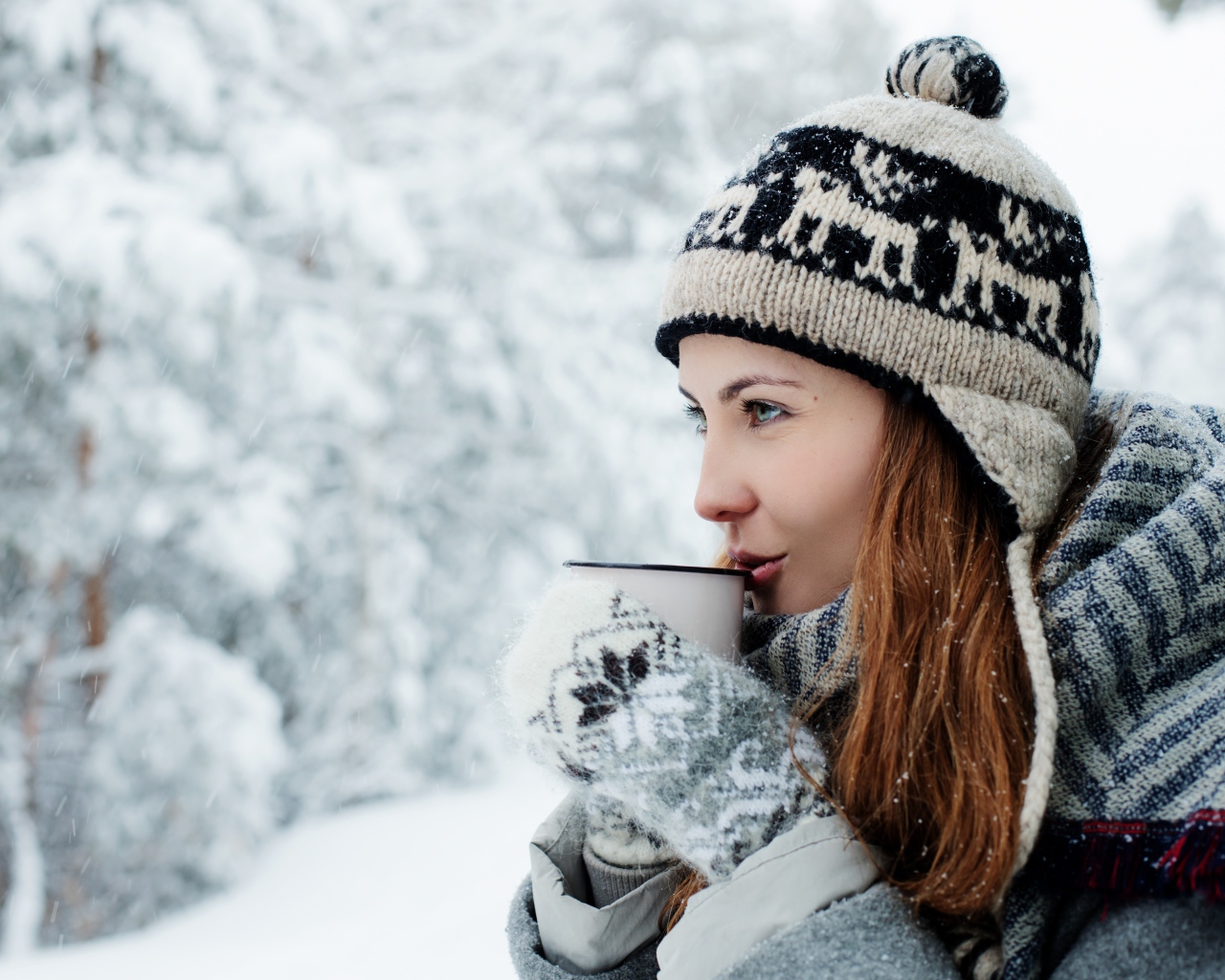 Красивая девушка в теплой шапке пьет кофе зимой на улице 