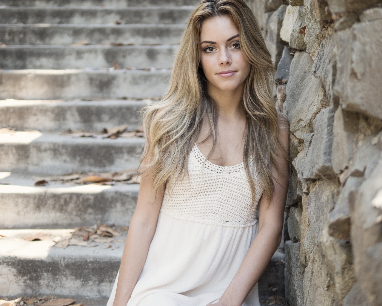 Красивая девушка в белом платье у каменной стены 