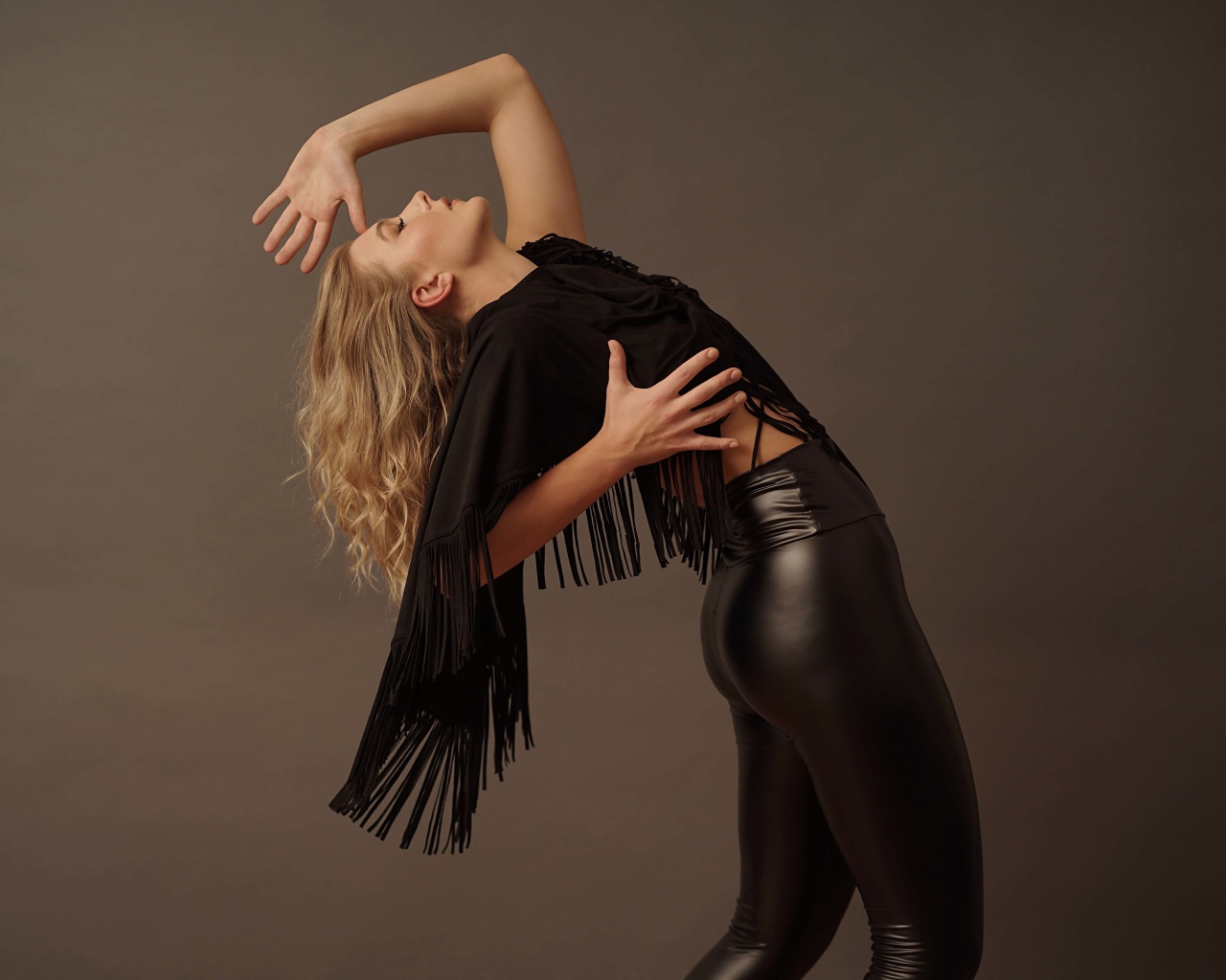 Красивая девушка в черных кожаных брюках на сером фоне