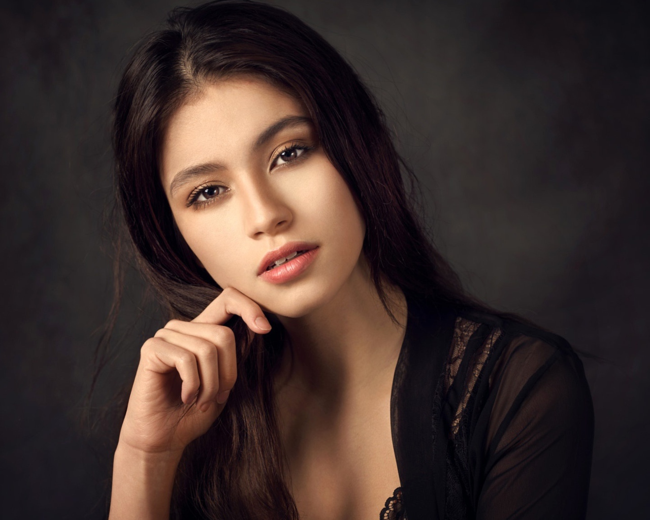 Красивая девушка в черном сидит на сером фоне