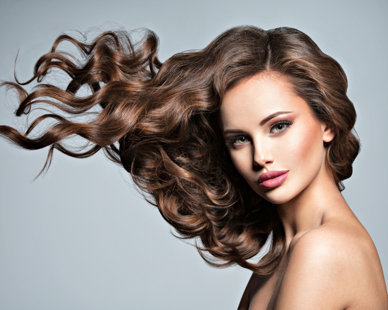 Красивая девушка модель с волнистыми волосами на сером фоне