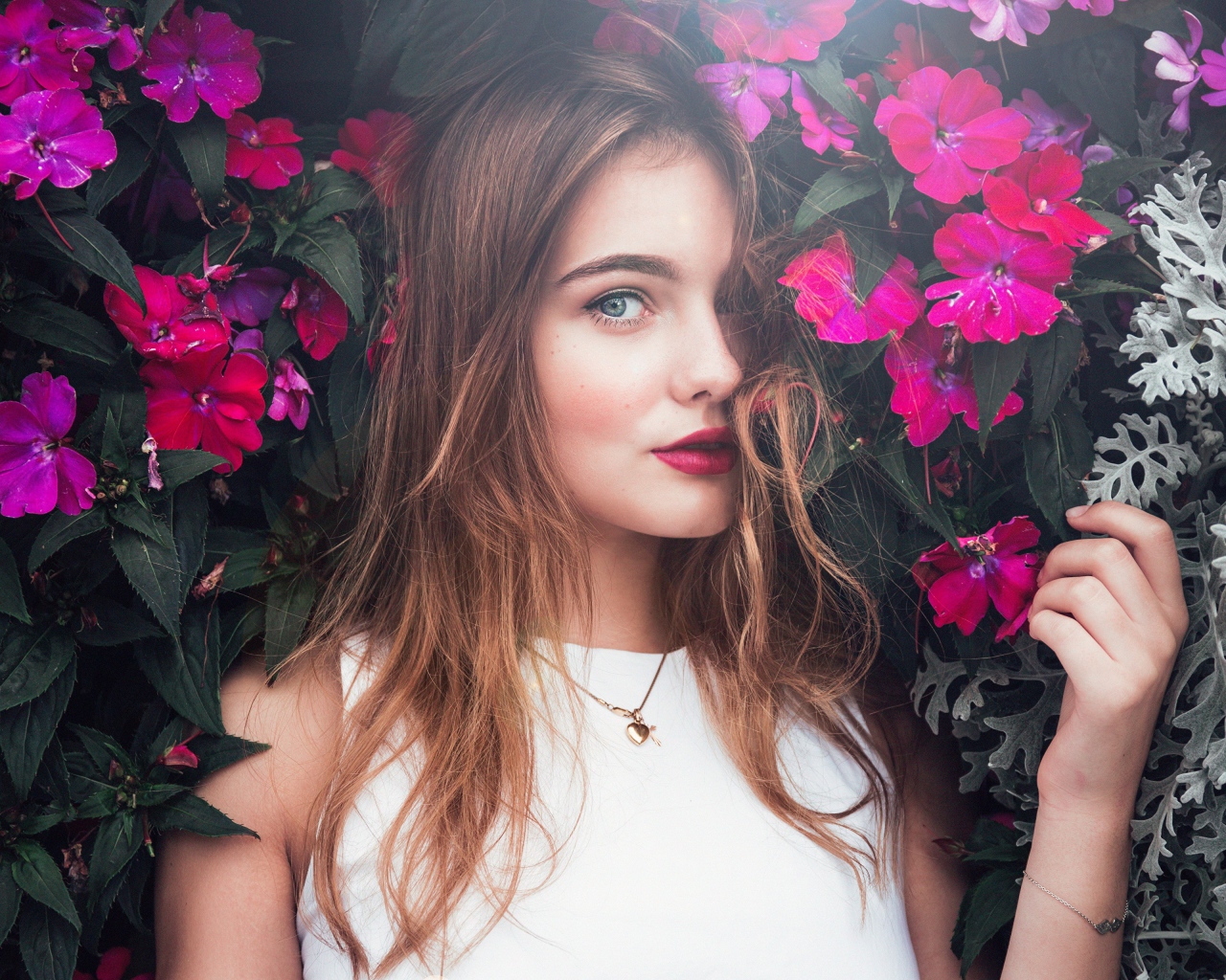 Красивая девушка стоит у зарослей с розовыми цветами