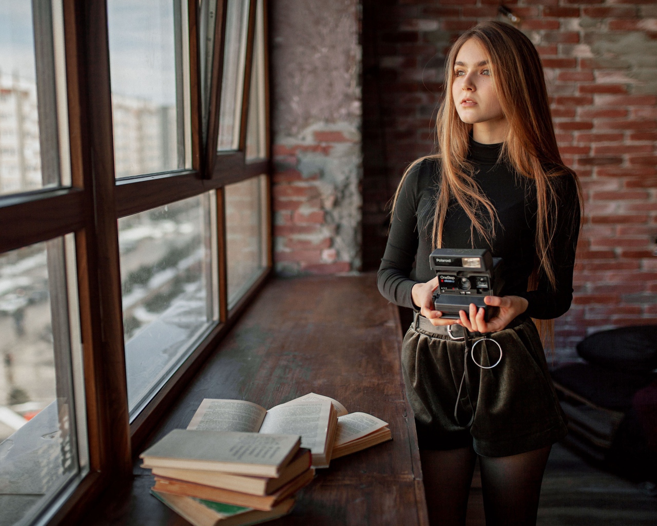 Красивая девушка с фотоаппаратом в руках у окна 