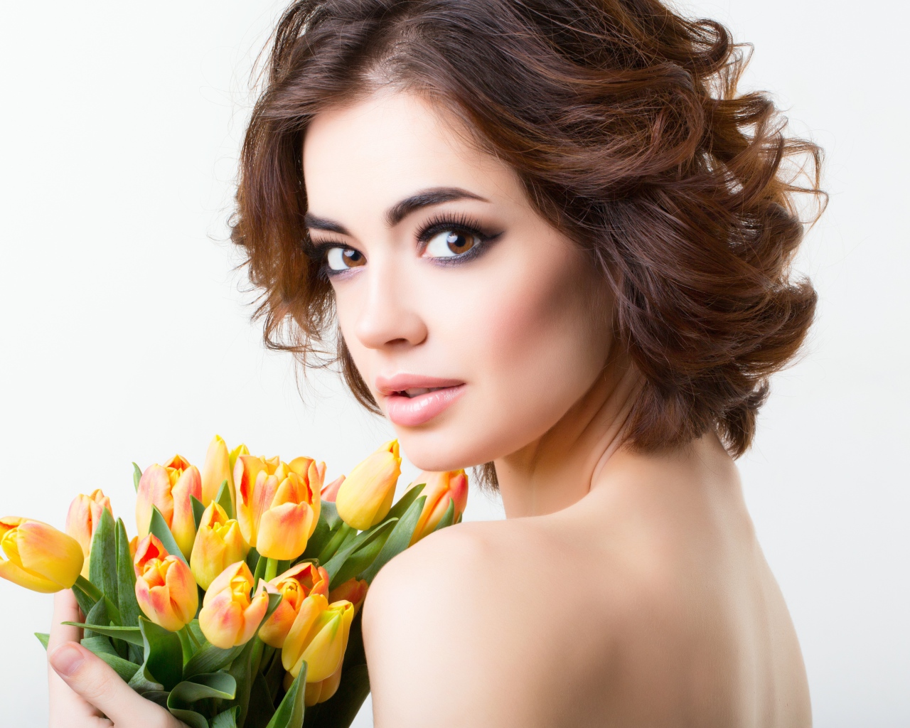 Красивая девушка с прической в букетом тюльпанов в руках на белом фоне