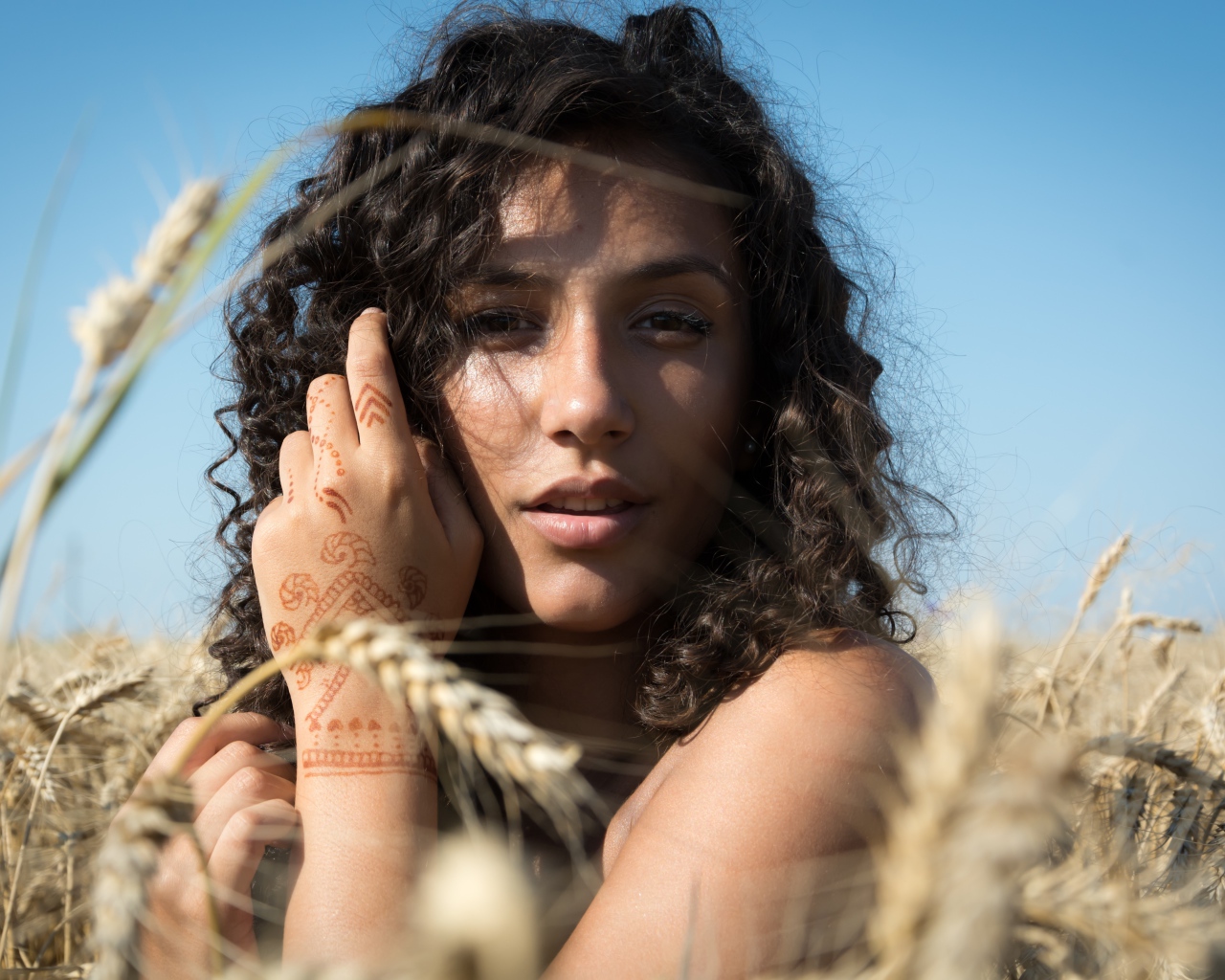 Красивая девушка с рисунком мехенди на руке на пшеничном поле 