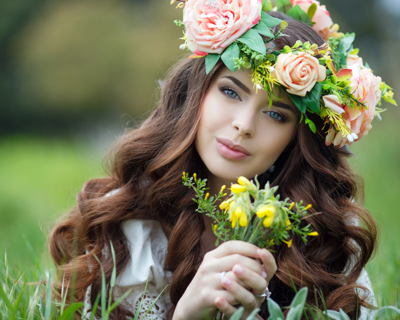 Красивая девушка с венком на голове лежит на зеленой траве