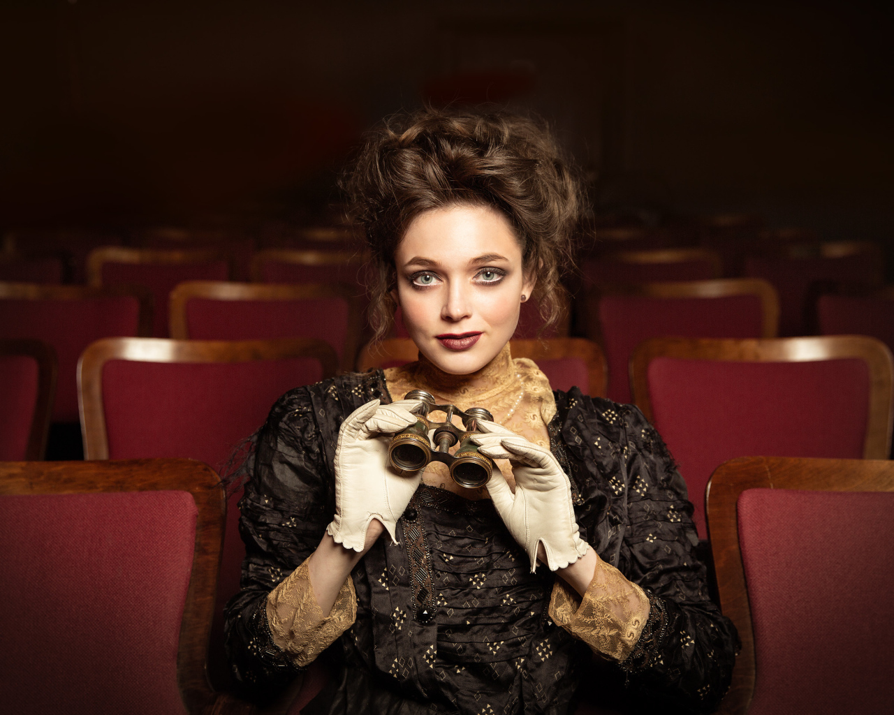 Красивая девушка с биноклем сидит в театре