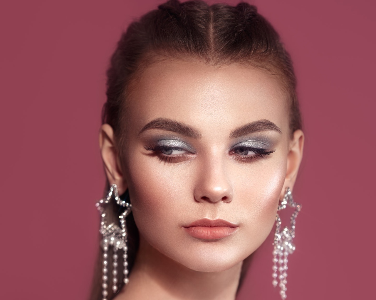 Красивая девушка с макияжем и большими серьгами на розовом фоне