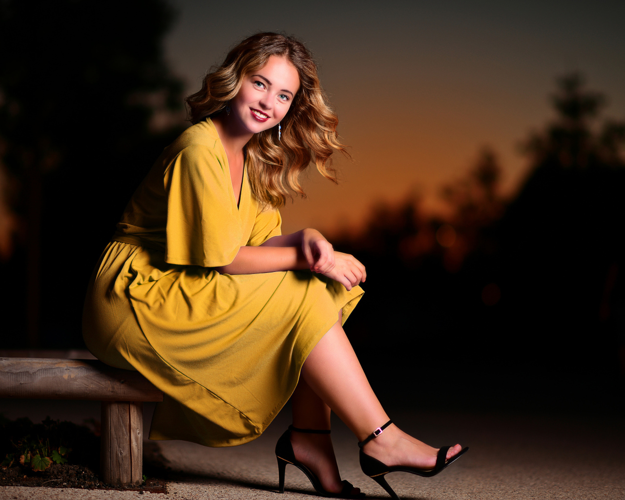 Красивая улыбающаяся девушка в желтом платье сидит на лавке 