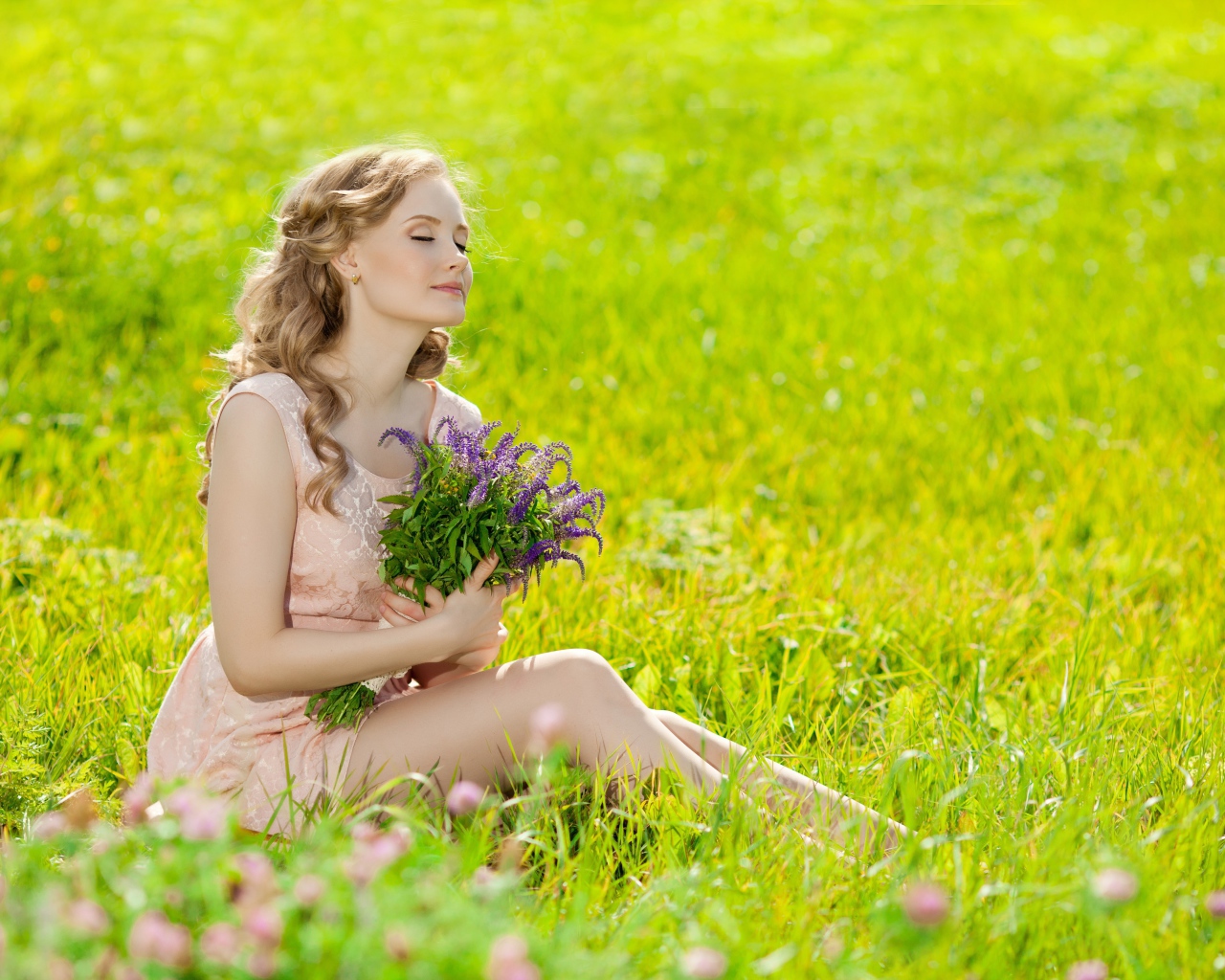 Красивая молодая девушка с букетом цветов сидит на зеленой траве