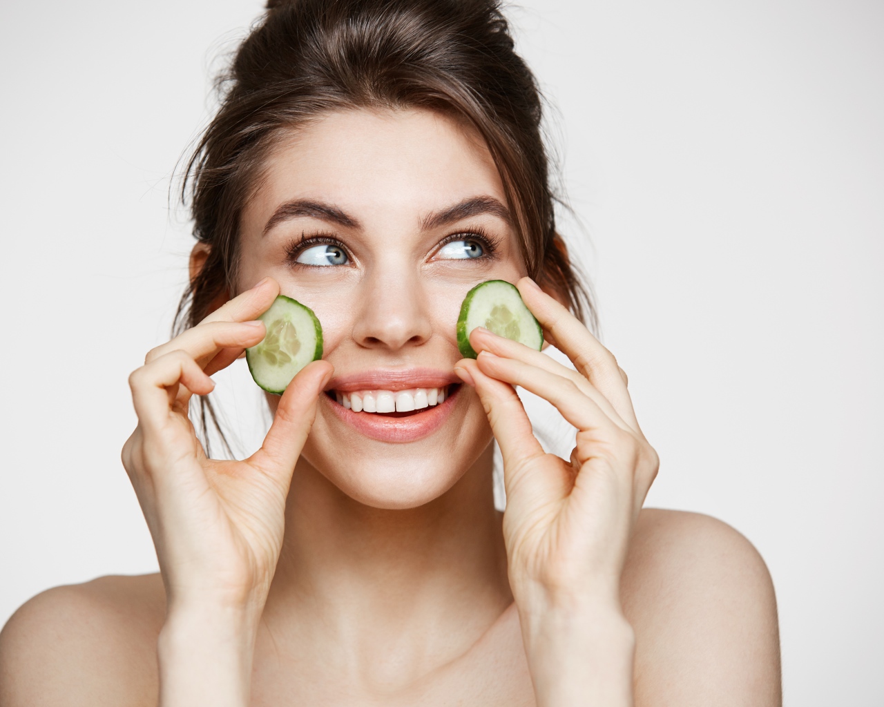 Голубоглазая девушка прикладывает огурцы к лицу 