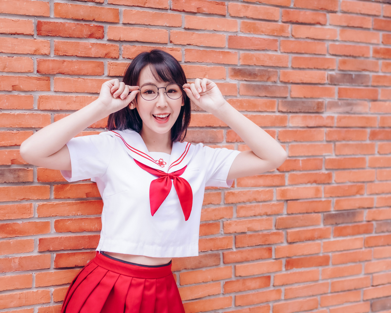 Яркая веселая азиатка в очках у кирпичной стены