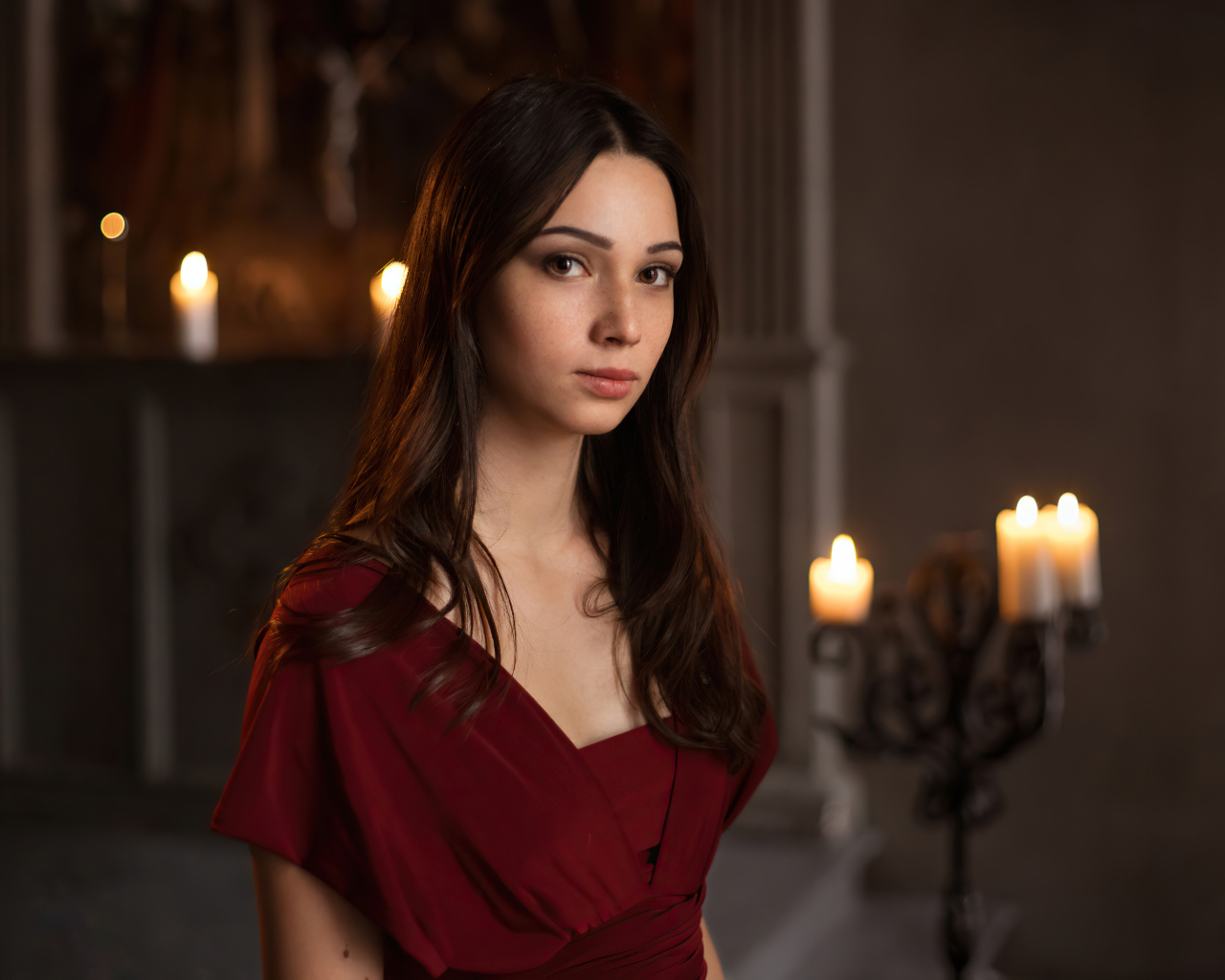 Кареглазая девушка в красном платье в комнате со свечами